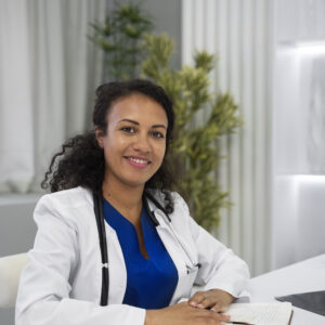 Docteur souriant avec un stéthoscope assis à son bureau, symbolisant l'approche chaleureuse et professionnelle du télésecrétariat médical.